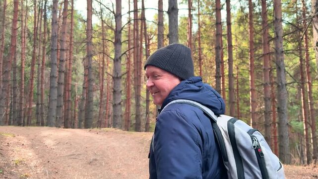 Senior smiling man hiking in pine forest wearing warm clothes and backpack