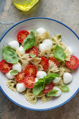 Caprese pasta salad with mini mozzarella balls, cherry tomatoes and farfalle served in a white and blue plate, middle close-up, elevated view