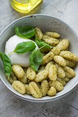 Bowl of italian potato gnocchi with basil oil, mozzarella cheese and basil leaves, vertical shot on a grey granite background, middle closeup