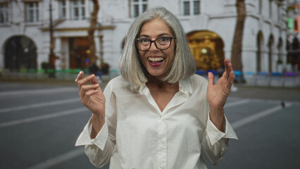 Fototapeta premium Woman smiling with hands raised showing open palms on street in front of arched building and benches; joy spontaneity.