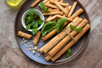 Various breadsticks, basil oil and fresh green basil on a brown plate, horizontal shot, high angle view, middle close-up