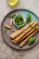 Plate with salted breadsticks grissini and basil oil on a beige granite background, vertical shot, high angle view