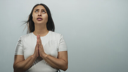 Fototapeta premium Woman with hands pressed together in prayer, eyes raised and bare hands visible in a light gray studio setting; hope devotion.