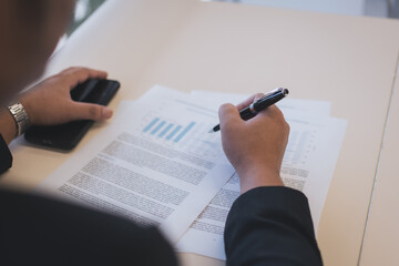 Businessman analyzing financial documents and charts with a smartphone, concept for finance, investment, planning, data analysis, and corporate decision-making.