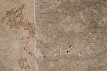 Close-up of aged stone wall with natural texture, cracks, and fossilized patterns in neutral beige tones