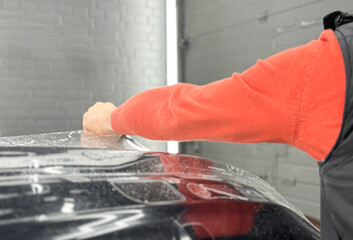 Car wrapping, detailing, tuning and styling. Detailer smoothes PPF. PPF protective film against chips and scratches. A car wrapping specialist applies a polyurethane film to the car. Selective focus.