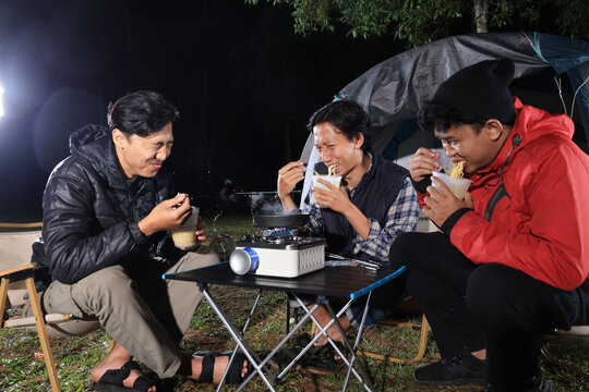 Asian Male Friend Eating Ramen Instant Noodle Cup in front of Camping Tent
