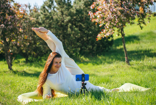 Woman doing yoga in park, stretching, recording video. - Powered by Adobe