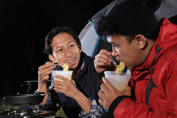 Young Asian Male Friend Eating Ramen Instant Noodle Cup in front of Camping Tent