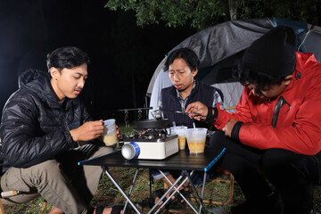 Three Young Asian Man Cooking Instant Noodel Cup in front of Camping Tent