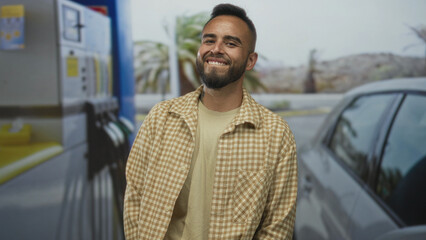Man smiling beside car near petrol pumps at a street gas station, looking up slightly with relaxed...