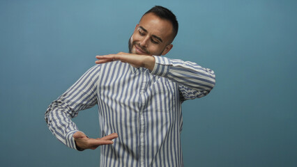 Man framing an invisible object with hands and smiling in a studio against a teal blue backdrop; confidence presentation.