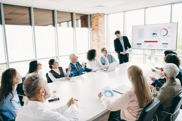 Diverse team gathers around a conference table in a modern office, collaborating over charts and...