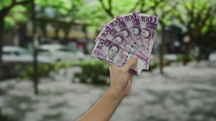 Man holding philippine pesos on a city street, showcasing purple banknotes against a blurred...