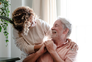 Elderly man smiling warmly holding hands of a caregiver woman indoors. The scene captures...
