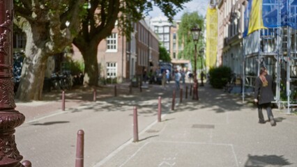 Obraz premium City street scene with a woman walking amidst blurred buildings and trees, capturing a warm european ambiance with defocused, bokeh-filled background highlighting urban architecture.