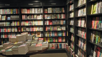 Blurred image showcasing an indoor library with stacked books on a table and shelves filled with colorful, defocused texts creating a bokeh effect.