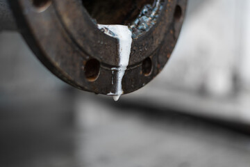 From the flange of the rusty pipe flows a white bubbly liquid of clearly chemical origin. High quality photo