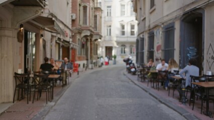 Narrow cobblestone street cafe scene shown in soft bokeh and defocused focus for an outdoor street setting; background, backdrop, copyspace, overlay.