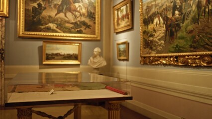Museum gallery defocused background showing framed paintings, a bust and a glass display case; background backdrop copyspace backplate.