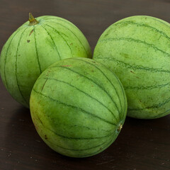 Three small green watermelons on a dark surface