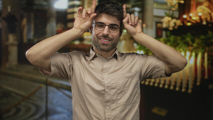 Fototapeta premium Young hispanic man showing rock horns with hands in church building; playful energy youthful spirit.