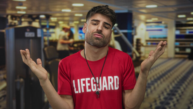 Man holds open palms amid treadmill rows in gymnasium with red lifeguard shirt and whistle around neck; uncertainty.