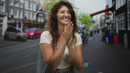 Woman clapping hands and smiling on street in white crop top and jeans, fists raised and pearl necklace visible by collarbone; celebration joy.