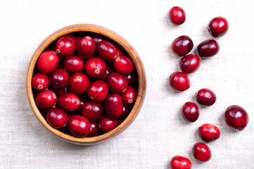 Fresh cranberries, bearberries, or American cranberries, in a wooden bowl, on linen. Ripe, bright red, large cranberries, Vaccinium macrocarpon, with shiny skin and acidic taste. Close-up, from above.
