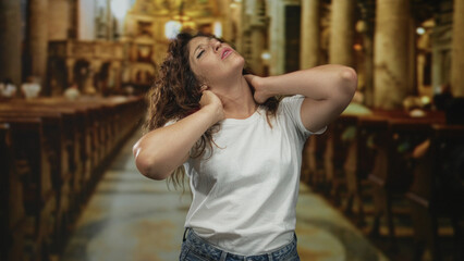 Woman clutching neck and tilting head back in church building with hands on neck and pained expression with neckache; prayer seeking distress.