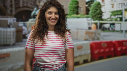 Woman smiling with bare forearms standing near construction barriers at building; confidence resilience community.