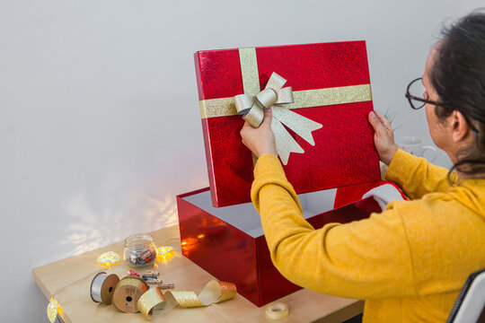 Woman preparing a Christmas gift box with red wrapping and decorative ribbon