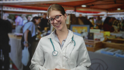 Young blonde woman wearing stethoscope with hand on chin in crowded street market; thoughtful focus.