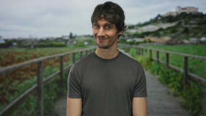 Man smiling showing face on a green park walkway beside a wooden fence and lush foliage; serenity calm contentment.