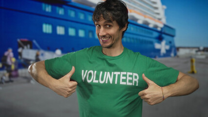 Fototapeta premium Young man pointing finger to volunteer shirt in front of large ship at port terminal; community spirit.
