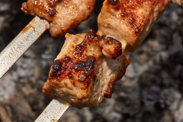 Large pieces of pork being grilled on skewers over hot charcoal. Delicious barbecue with a golden crust cooking outdoors during a picnic or countryside gathering.
