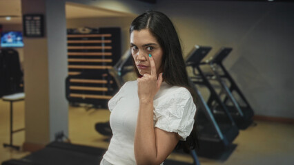 Woman points finger to eye in gym with a stern watchful gaze and direct pointing gesture toward...