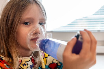 Child using asthma inhaler with spacer mask for respiratory therapy, concept of pediatric asthma and home treatment