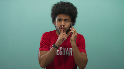 Lifeguard man with smartphone asks for silence against a green background, emphasizing a serious...