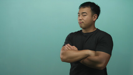 Fototapeta premium Man with arms crossed in green studio setting wearing a fitted black t shirt and looking to the side; confidence pride strength determination.