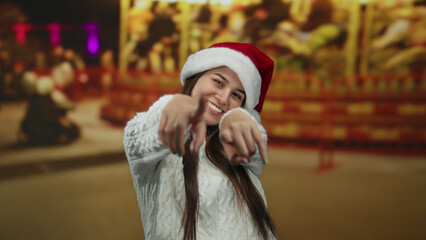 Woman wearing santa hat smiles in amusement park with holiday lights in background enjoying festive...