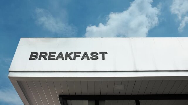 Breakfast word sign clearly displayed on the exterior of a cafe or restaurant building beneath a bright blue sky, signifying an establishment offering morning meals and early dining service
