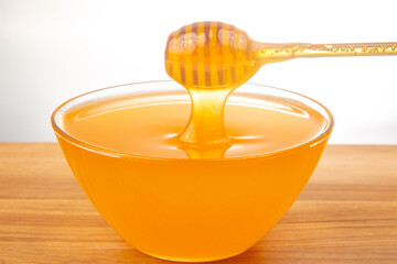 Golden honey drips from a wooden dipper into a glass bowl on a wooden surface