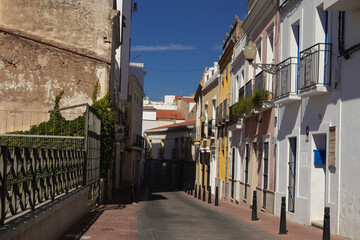Calle tradicional y estrecha en el centro histórico de Mérida, Extremadura, España, con fachadas antiguas, balcones y bolardos.