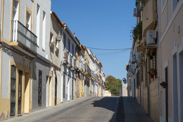 Calle tradicional de Mérida, España, con edificios antiguos y balcones. La perspectiva de la calle empedrada se pierde en el horizonte bajo un cielo azul despejado.