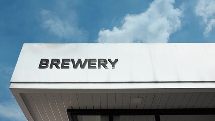Brewery word sign boldly displayed on the industrial or rustic facade of a manufacturing building beneath a clear blue sky, signifying beer production, craft brewing, and local beverage creation