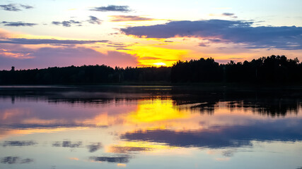 Colorful sunset over a tranquil lake surrounded by silhouettes of trees
