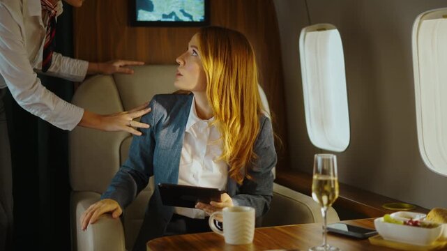 Frightened businesswoman feeling scared and anxious during unexpected severe turbulence on a luxury private jet, while a flight attendant tries to calm her down during the bumpy flight