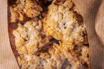 A close-up of golden brown oatmeal cookies seen through a transparent window in a  paper bag. Textured and crumbly appearance.