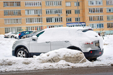 Frozen suv buried under piles of snow after blizzard and street cleaning operation in cold urban environment. Snow covered car along residential building street, aftermath of municipal snow removal